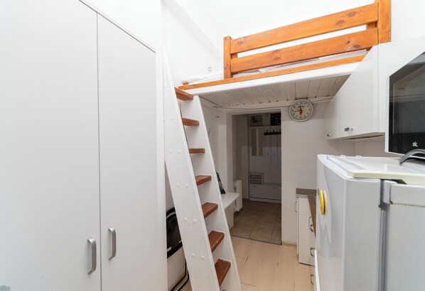 A narrow hallway with a wooden loft bed, a white refrigerator, and a clock on the wall. - Standard Studio with Mezzanine (Wrocław)