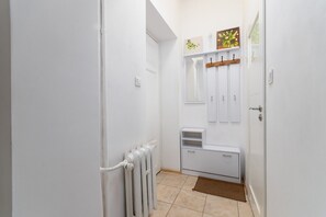 A narrow hallway with white walls, a radiator, a small white cabinet, and a brown rug on the floor. - Standard Studio with Mezzanine (Wrocław)