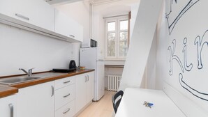 A compact kitchen with white cabinets, a wooden countertop, a sink, a kettle, a refrigerator, and a window with a view of buildings outside.