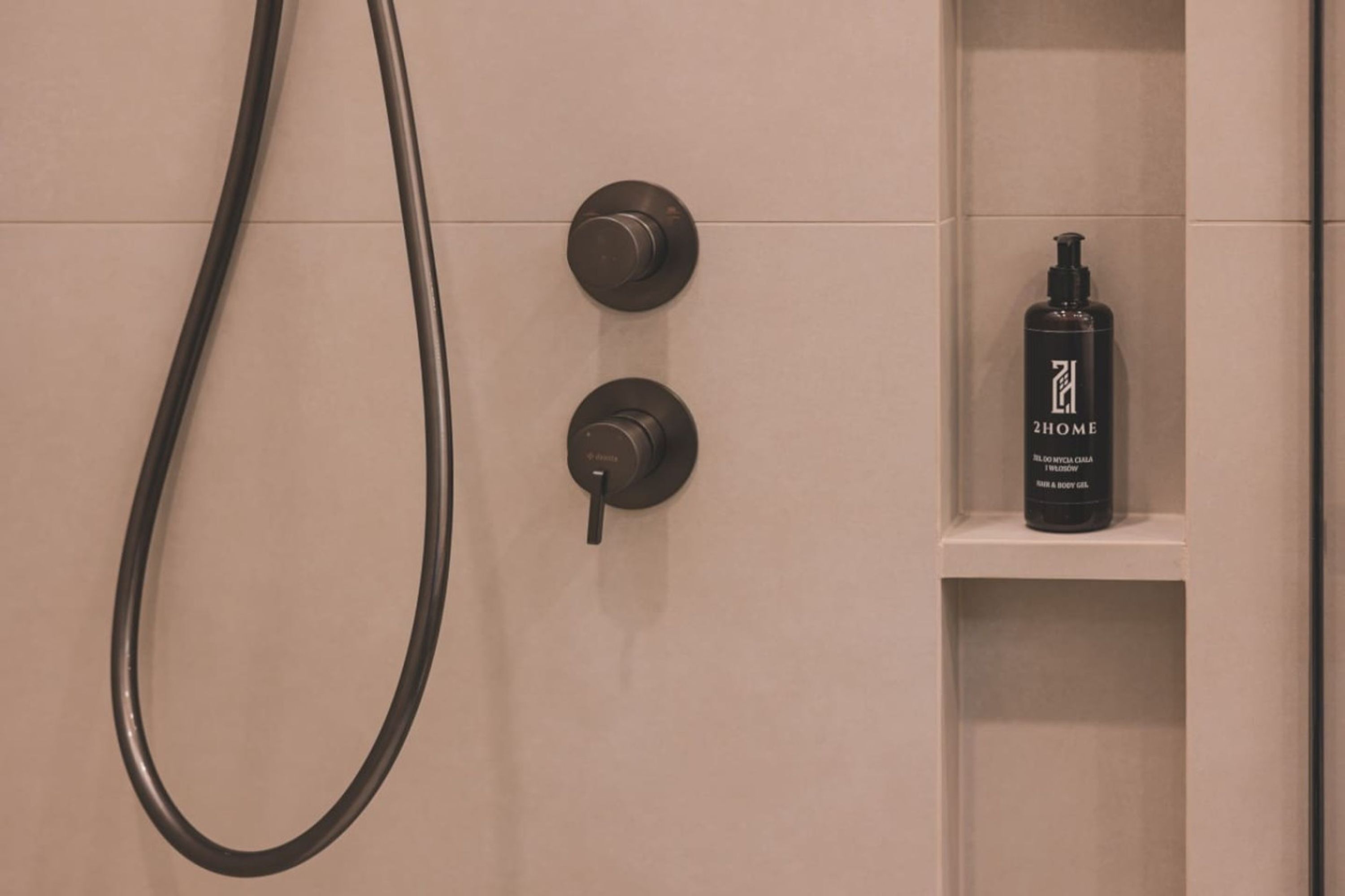 A bathroom with a shower, two towel racks, and a shelf with a bottle of body lotion.