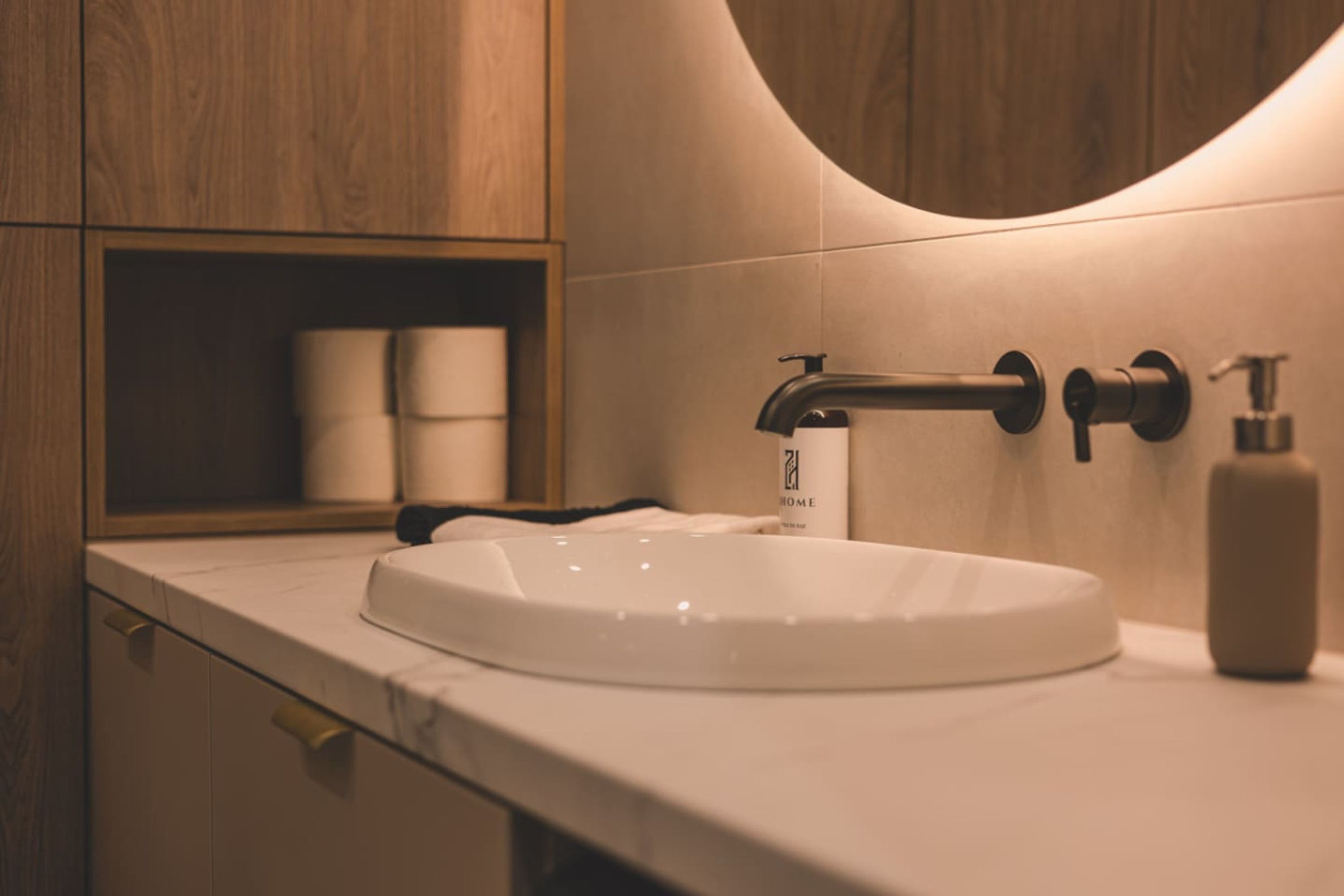 A modern bathroom with a white sink, a wooden cabinet, and a towel dispenser.