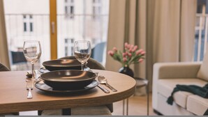A dining table set with plates, cutlery, and wine glasses, with a view of a building and a vase of flowers in the background. - Puerto 7 Stylowe Studio z Tarasem Doskona y Komfort (Bydgoszcz)
