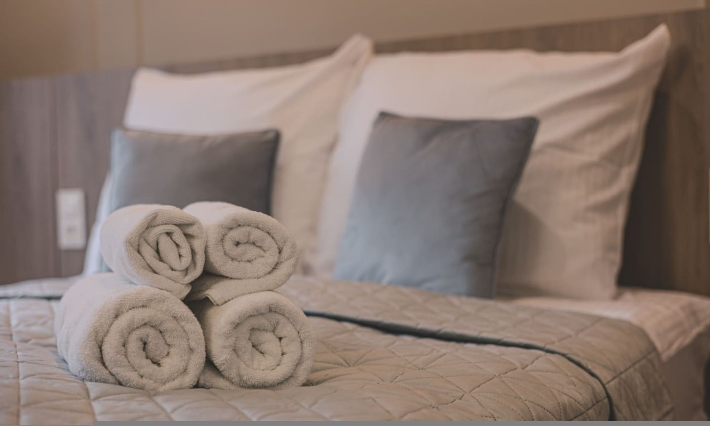 A neatly made bed with rolled towels and pillows.