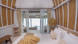 Un'ampia camera da letto con un letto grande, una panca in legno e vista sulla spiaggia attraverso delle vetrate.
