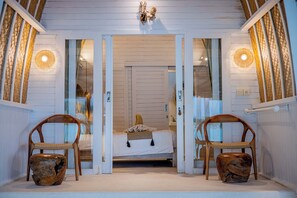 Quarto com cama, duas cadeiras de madeira e uma luminária de parede singular.