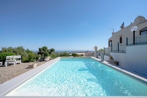 Ein rechteckiger Swimmingpool mit klarem Wasser, umgeben von einer weißen Poolterrasse, einer weißen Bank und einer Topfpflanze.