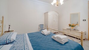Un dormitorio con cama, mesita de noche, silla, armario, espejo y cómoda.