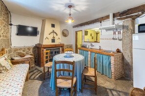 A cozy room with a bed, a dining table with chairs, a fireplace, a television mounted on the wall, and a kitchen area with a refrigerator and microwave. - Country House 'Tu Casa' with Wi-Fi (La Iglesuela)