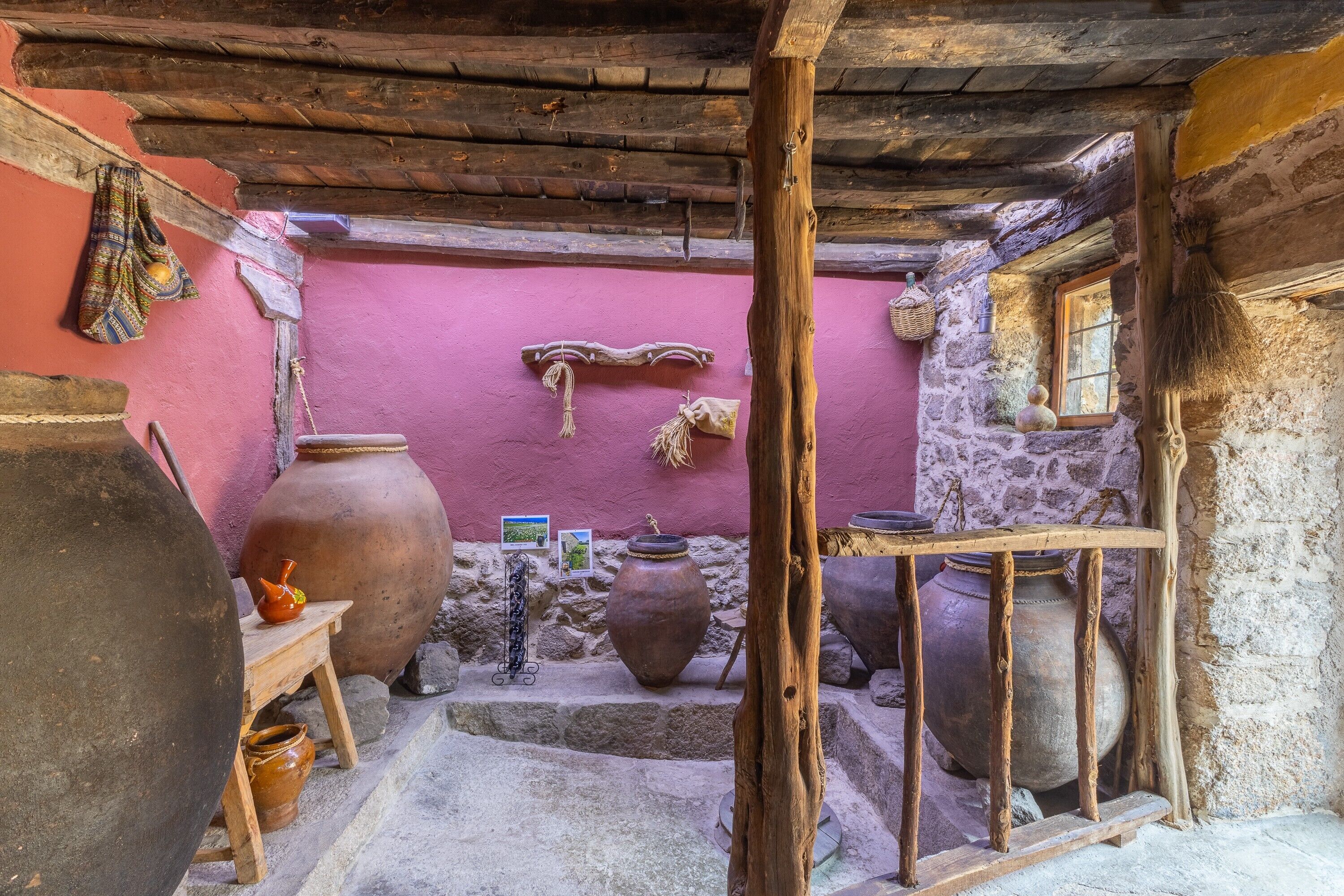 A rustic interior with large pottery, a wooden bench, and a stone wall.