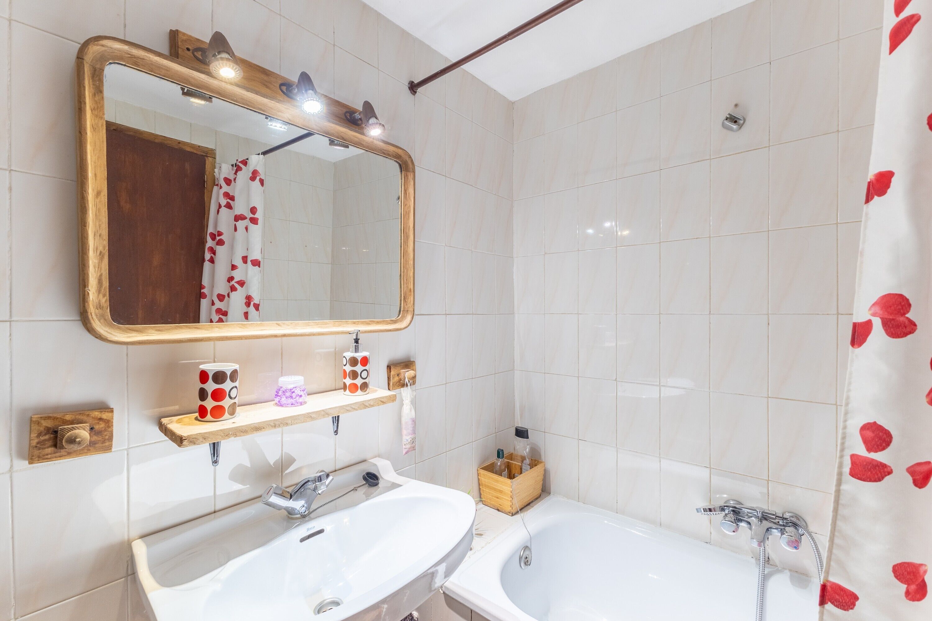 A bathroom with a large mirror, two sinks, a bathtub, and a shower curtain with red heart patterns.
