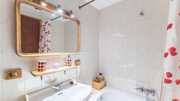 A bathroom with a large mirror, two sinks, a bathtub, and a shower curtain with red heart patterns.