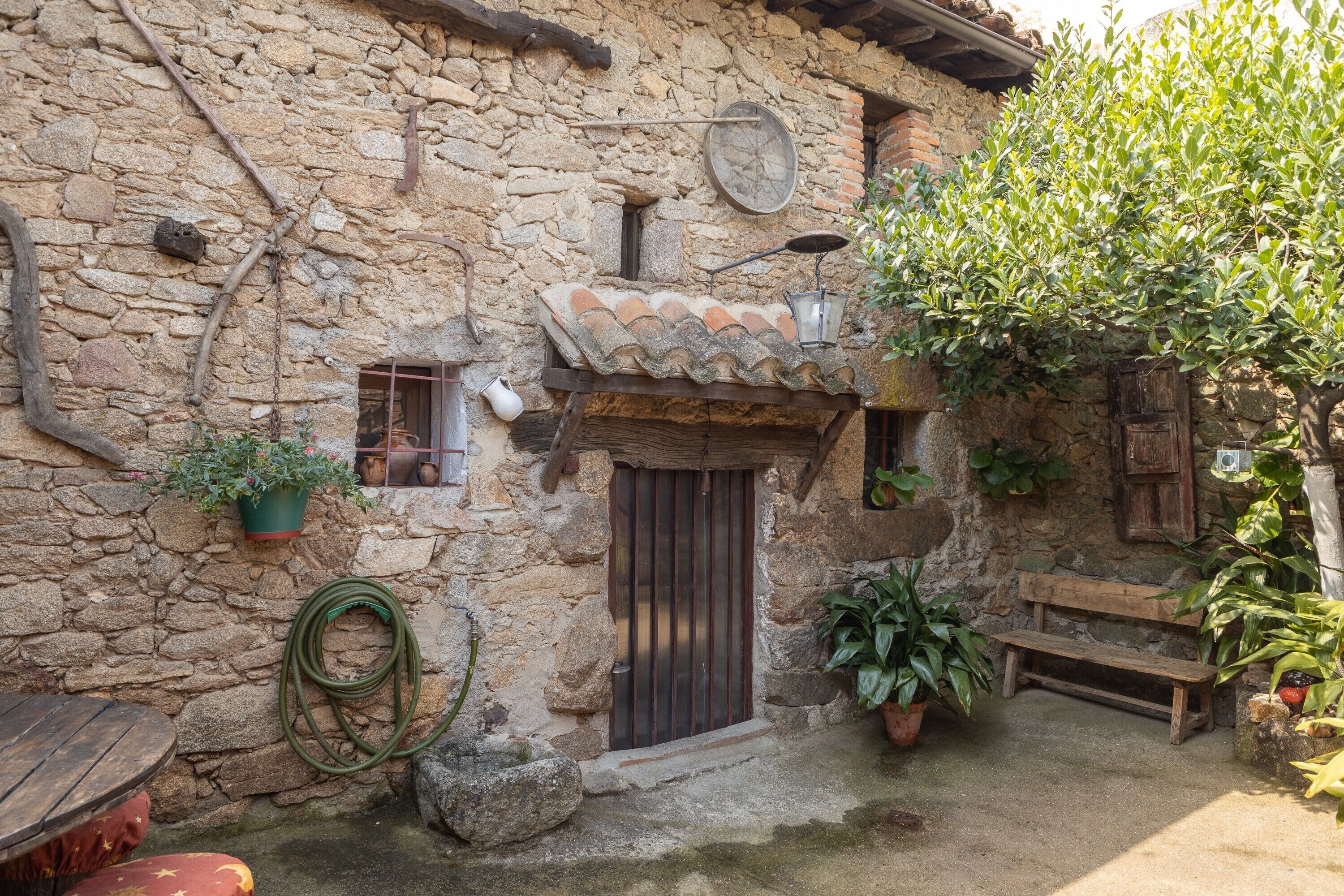 A rustic stone building with a tiled roof, a wooden bench, and potted plants.