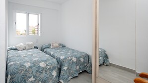 A bedroom with two beds, a window, and a wooden door.