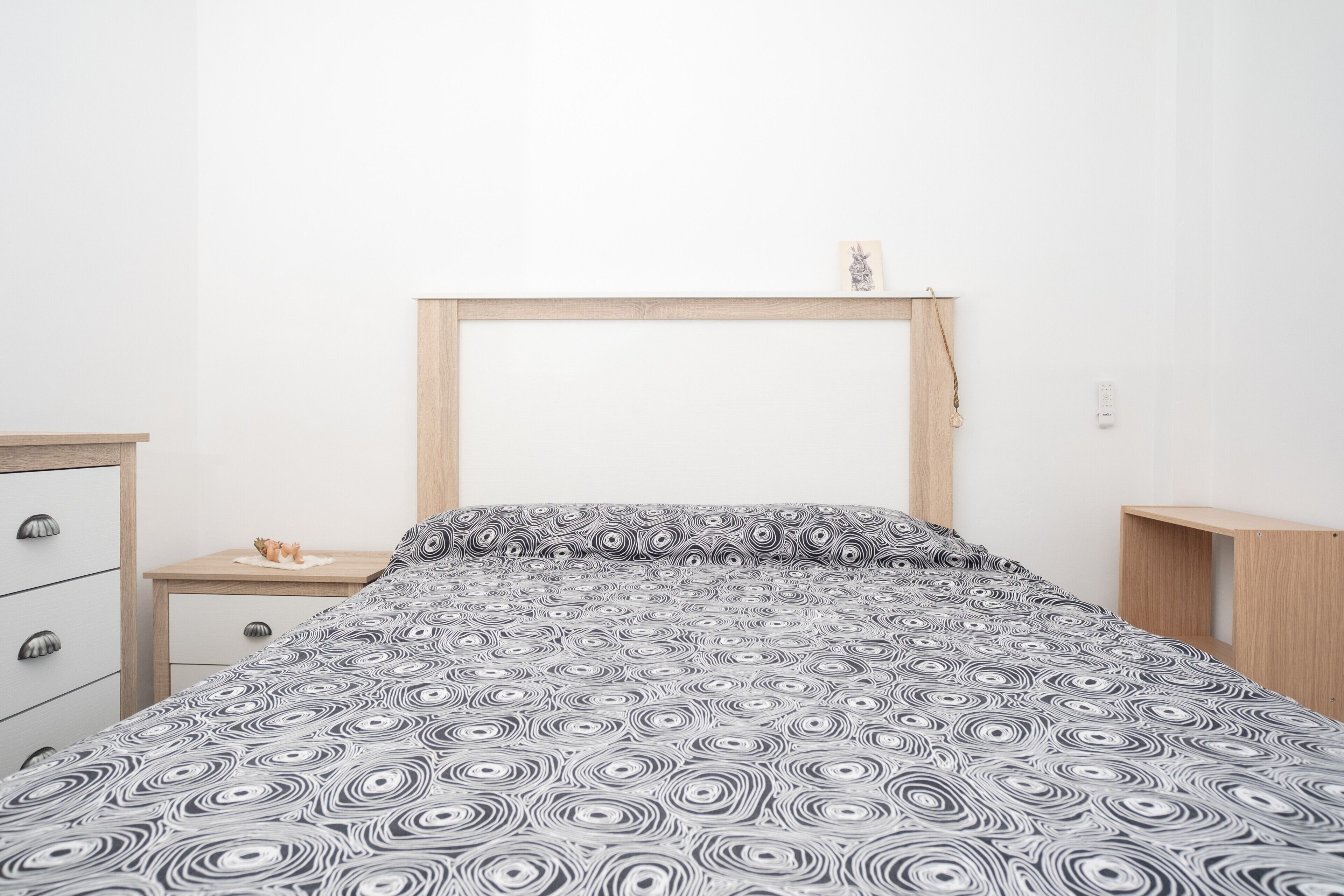 A bedroom with a bed, a wooden headboard, a bedside table, and a dresser.