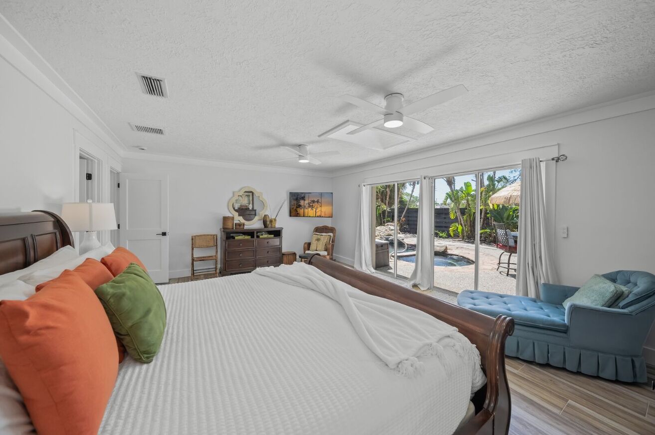 A spacious bedroom with a large bed, a ceiling fan, and a view of an outdoor pool area.