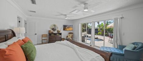 A spacious bedroom with a large bed, a ceiling fan, and a view of an outdoor pool area.