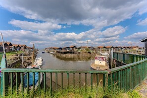 Een rivierdorpje met aan wal afgemeerde boten, houten huizen met rode daken en een groene metalen balustrade op de voorgrond.