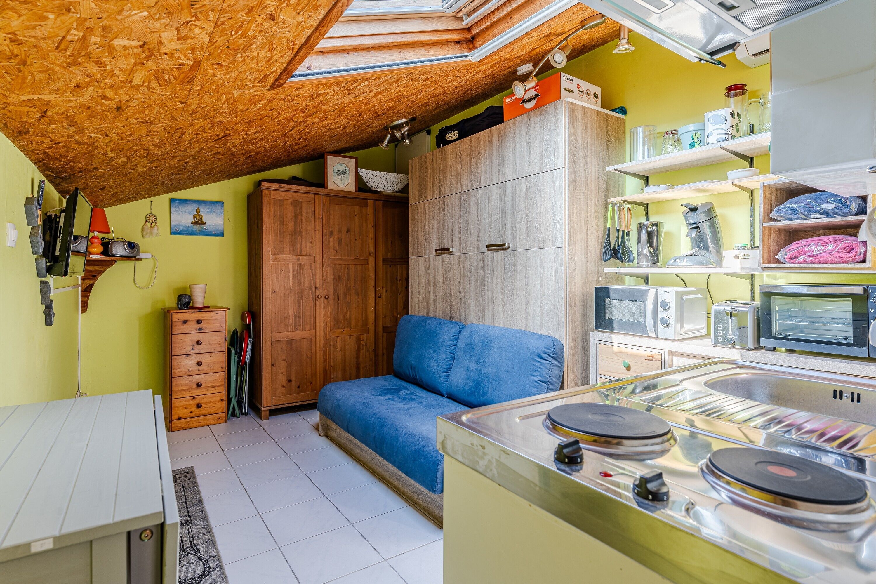 Eine kleine Küche mit Herd, einem blauen Sofa, Holzschränken und einem Oberlicht.