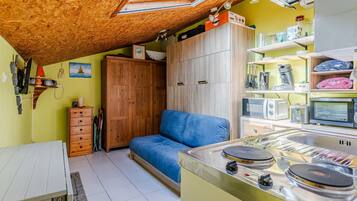 Eine kleine Küche mit Herd, einem blauen Sofa, Holzschränken und einem Oberlicht.