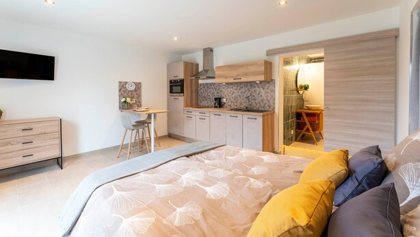 Un dormitorio moderno con cama, mesita de noche y vista a la cocina contigua.