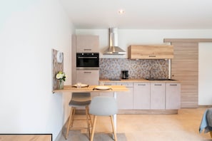 Una cocina moderna con horno empotrado, cafetera y zona de comedor con dos sillas.