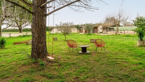 Un árbol, un columpio, dos sillas rojas y una mesa en un espacio al aire libre con césped.