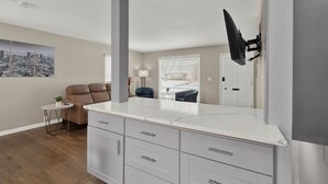 A modern kitchen with white cabinetry, a marble countertop, and a black hanging light fixture. - Birmingham Retreat - Work & Play (Birmingham)