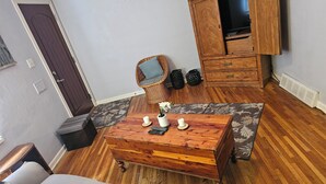 A living room with a wooden coffee table, a wicker chair, a sofa, a television on a wooden cabinet, and a door.