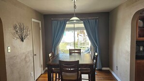 A dining area with a wooden table and chairs, a chandelier, and a view of the outdoors through curtains.