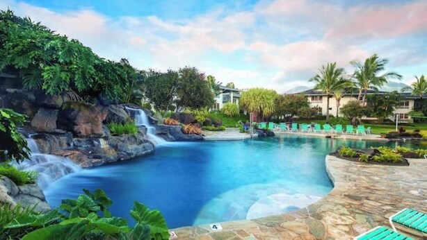 A resort pool with a waterfall, surrounded by lush greenery and palm trees. - Wyndham Bali Hai 3BR Suite with Resort Access (Princeville)