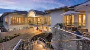 A modern multi-story hotel with a glass atrium, outdoor seating, and a landscaped courtyard. - Wyndham Bali Hai 3BR Suite with Resort Access (Princeville)