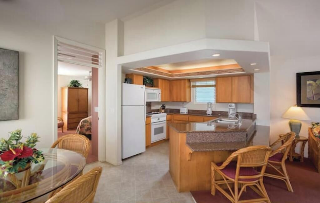 Una cocina compacta con armarios de madera, una isla central y un área de comedor con sillas de mimbre.