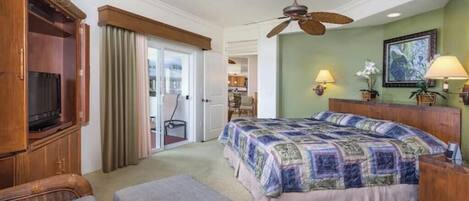 A hotel room with a large bed, a wooden wardrobe, a television, a ceiling fan, and a view of the adjacent room.