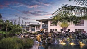 A modern building with a landscaped garden, a pond with a waterfall, and a sculpture. - Wyndham Bali Hai 3BR Suite with Resort Access (Princeville)