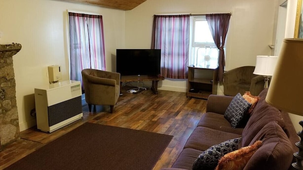 A living room with a brown sofa, a television, and a stone fireplace. - Hawthorne Cottages Chickadee Heights (Raymond)