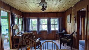 A wooden cabin interior with a dining table, chairs, a lamp, and a window with curtains. - Hawthorne Cottages Sand Castle (Raymond)