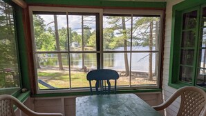 A room with a table and two chairs, a window with a view of a lake and trees, and a green-painted wall. - Hawthorne Cottages Sand Castle (Raymond)