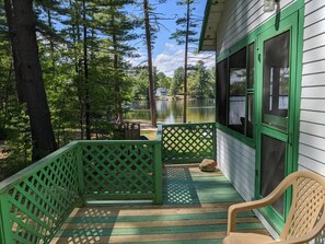 A wooden deck with green railings, a chair, and a view of a lake and a house in the background.