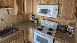 A kitchen with wooden cabinets, a white stove, a microwave, a sink, and a coffee maker. - Hawthorne Cottages Sand Castle (Raymond)