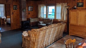 A cozy cabin interior with a fireplace, wooden walls, a sofa, and a dining area.