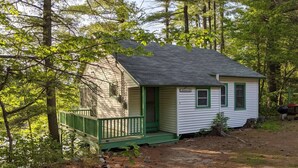 A small cabin with a green porch, surrounded by trees. - Hawthorne Cottages Edgewater (Raymond)