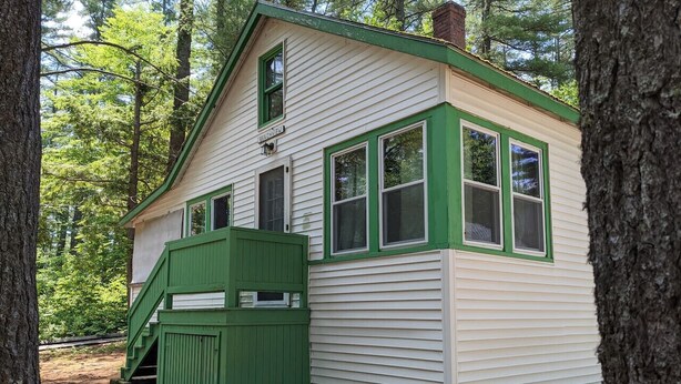 A small, single-story cabin with a green front porch and white siding, surrounded by trees. - Hawthorne Cottages Outpost (Raymond)