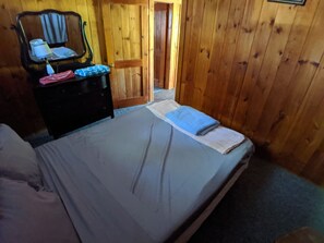 A wooden-paneled room with a bed, a dresser, and a mirror. - Hawthorne Cottages Overlook (Raymond)