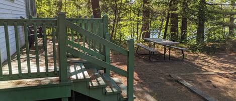 A wooden deck leading to a house, a picnic table, and a forested area.