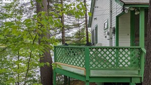 A wooden deck with a lattice railing, attached to a house with green trim and white siding. - Hawthorne Cottages Lakeside (Raymond)