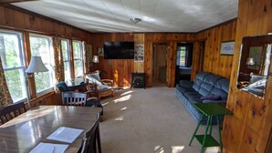 A wooden cabin interior with a dining area, sofa, and fireplace. - Hawthorne Cottages Lakeside (Raymond)