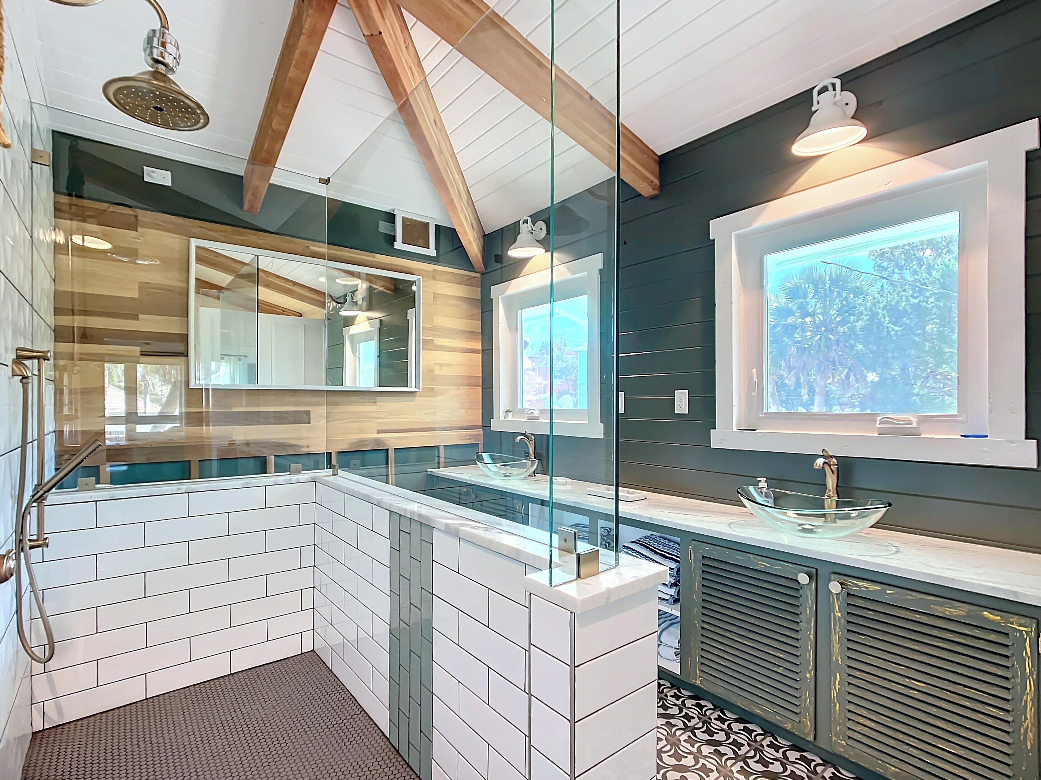 A modern bathroom with a glass shower enclosure, a large mirror, and a window providing natural light.