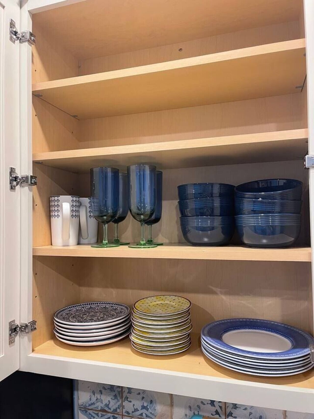 A cabinet with shelves containing stacked plates and blue glassware.