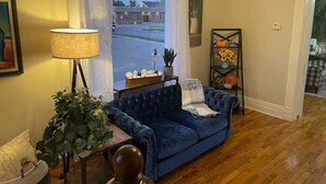 Een woonkamer met een blauwe bank, een lamp, een plant en uitzicht op een straat.
