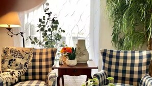 Een gezellige woonkamer met geruite banken, een kleine houten tafel met een bloemenvaas, en een grote potplant.